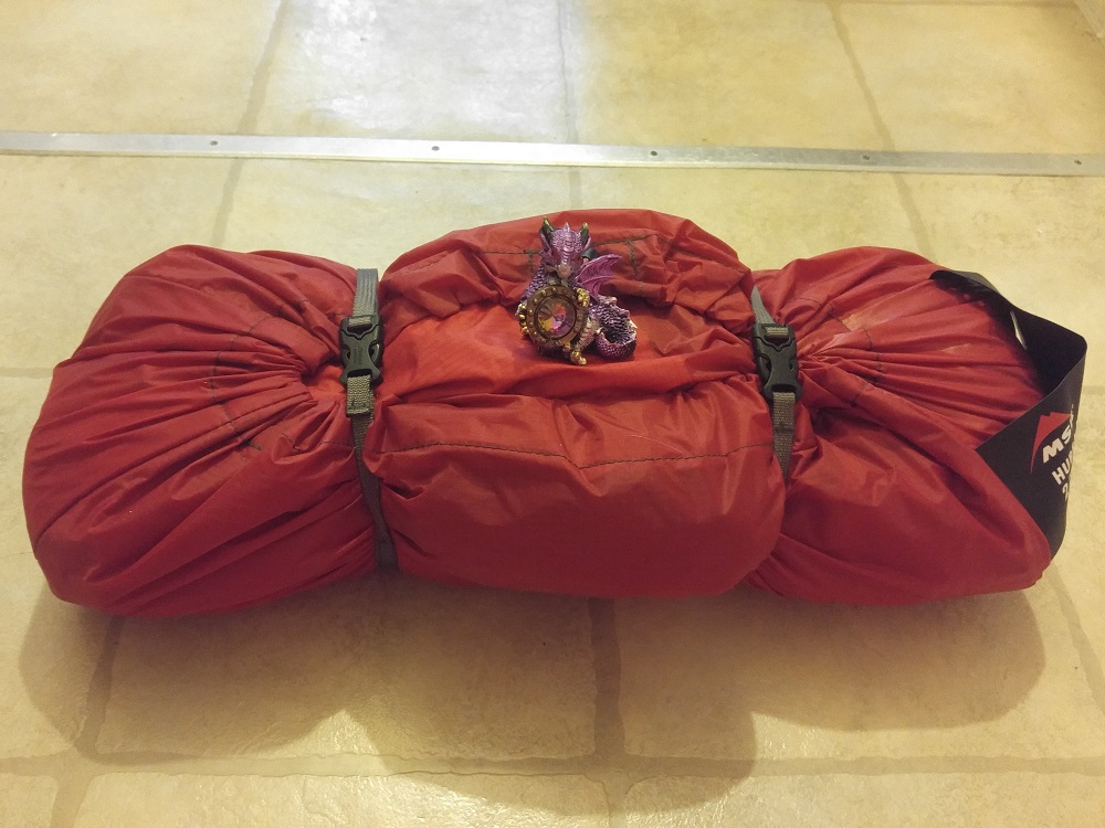 A small purple winged dragon statue holding a gemstone, sitting on top of a rolled up red tent.