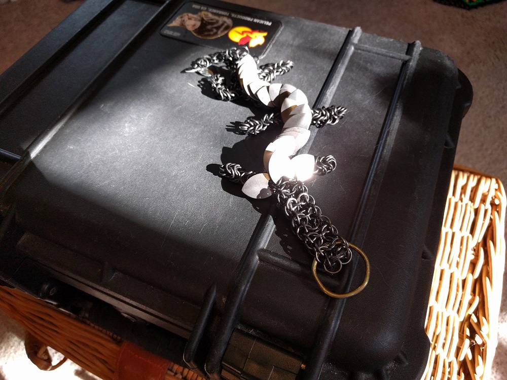 A six legged dark grey and silver striped dragon with black rings, sitting on a black plastic case in the sun.