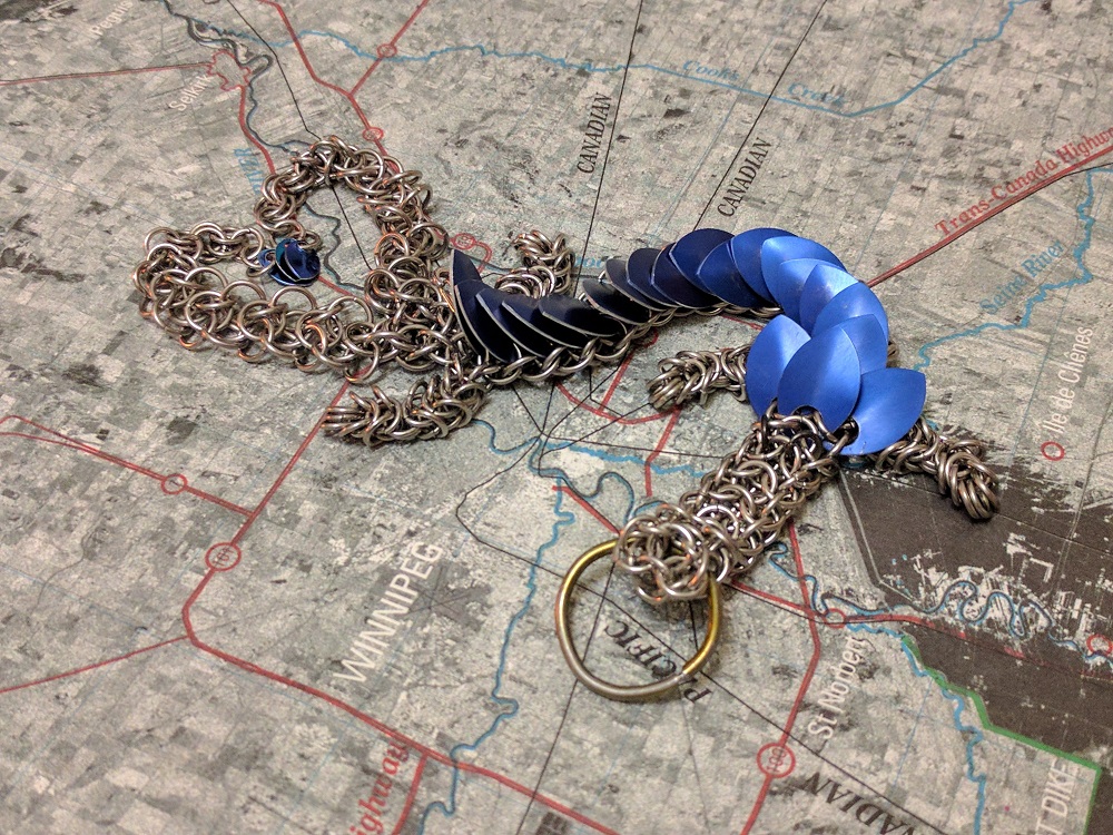 A two tailed blue dragon laying on a map, with the two tails forming a heart.