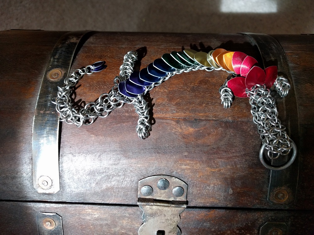 A rainbow striped dragon laying in the sun atop a wooden chest.