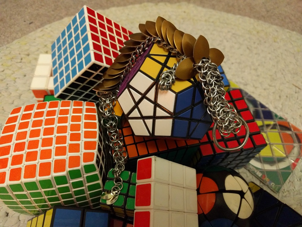 A brown dragon laying atop a pile of Rubik's and other twisty puzzle cubes on a white rug.