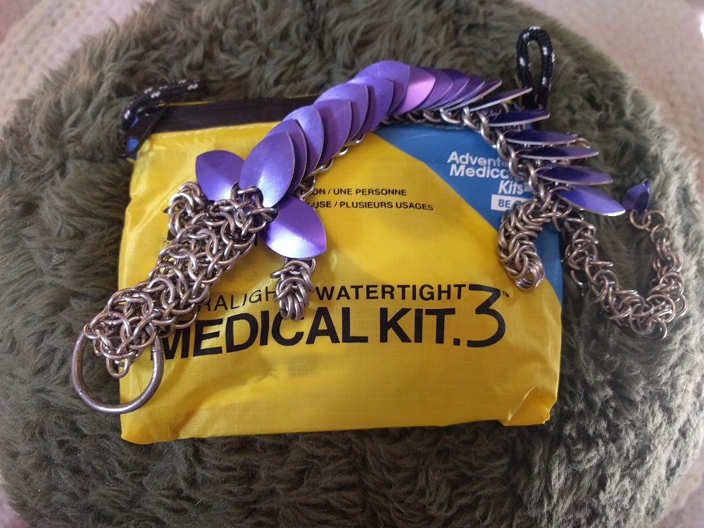 A purple dragon laying on top of a travel medical kit, atop a grey fuzzy fabric.