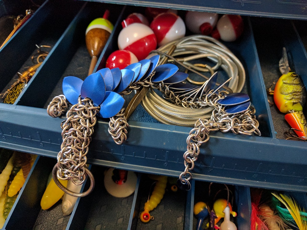 A blue dragon sitting inside of a blue tackle box with lures and floaters.