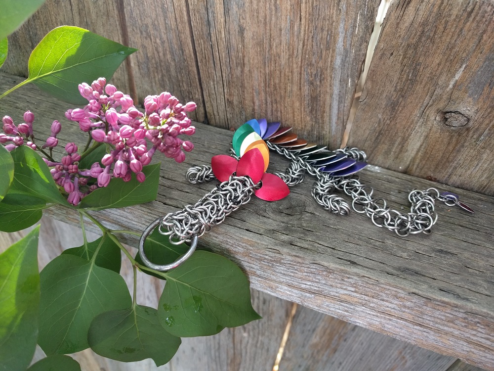 A double rainbow striped dragon laying on the crossbeam of a fence beside some budding lilac flowers.