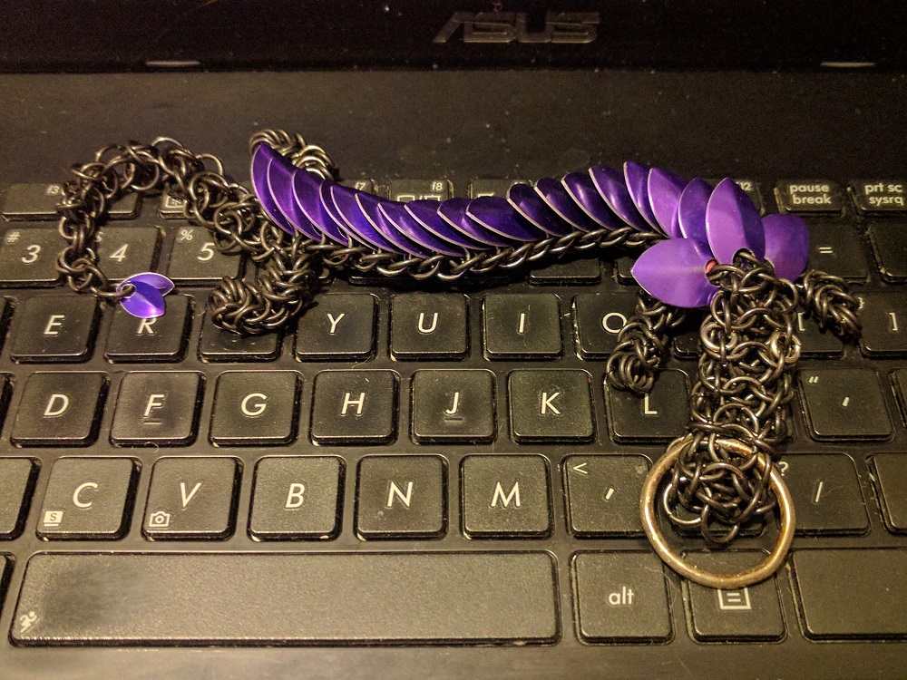 A purple dragon with black rings laying on top of the black keyboard of a laptop.