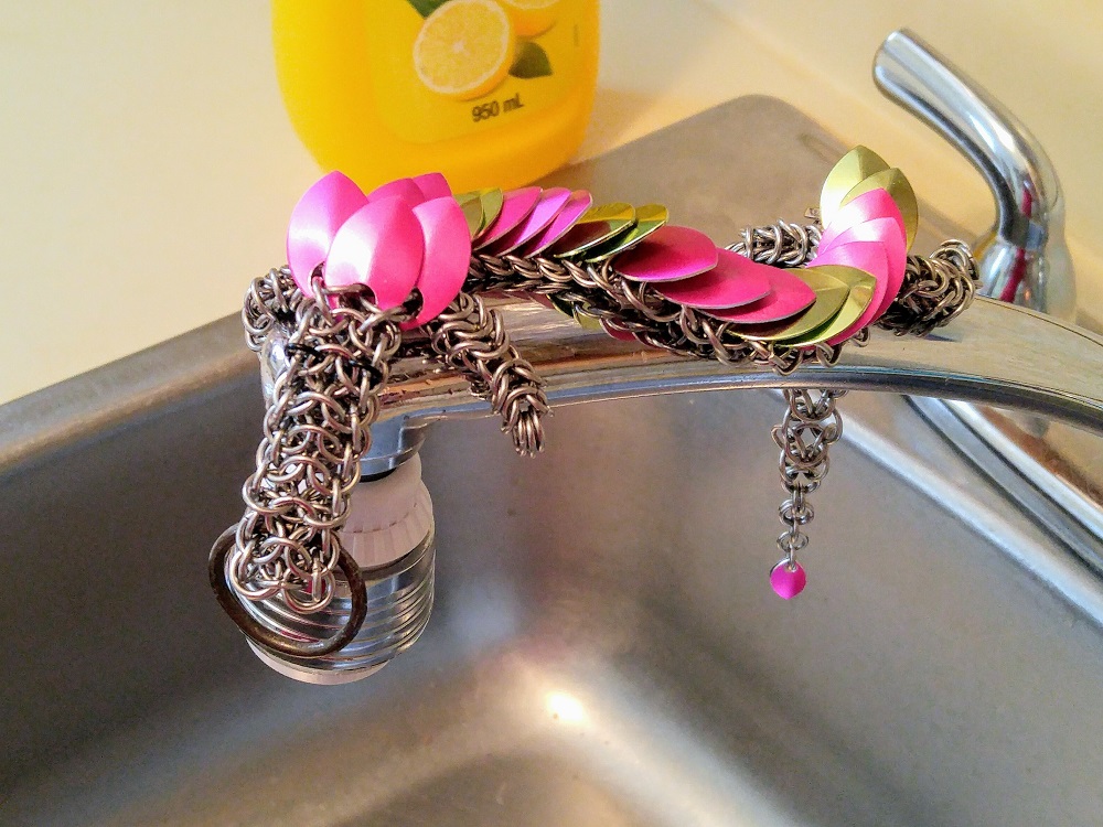 A bright pink and lime green dragon sitting on the faucet of a sink.