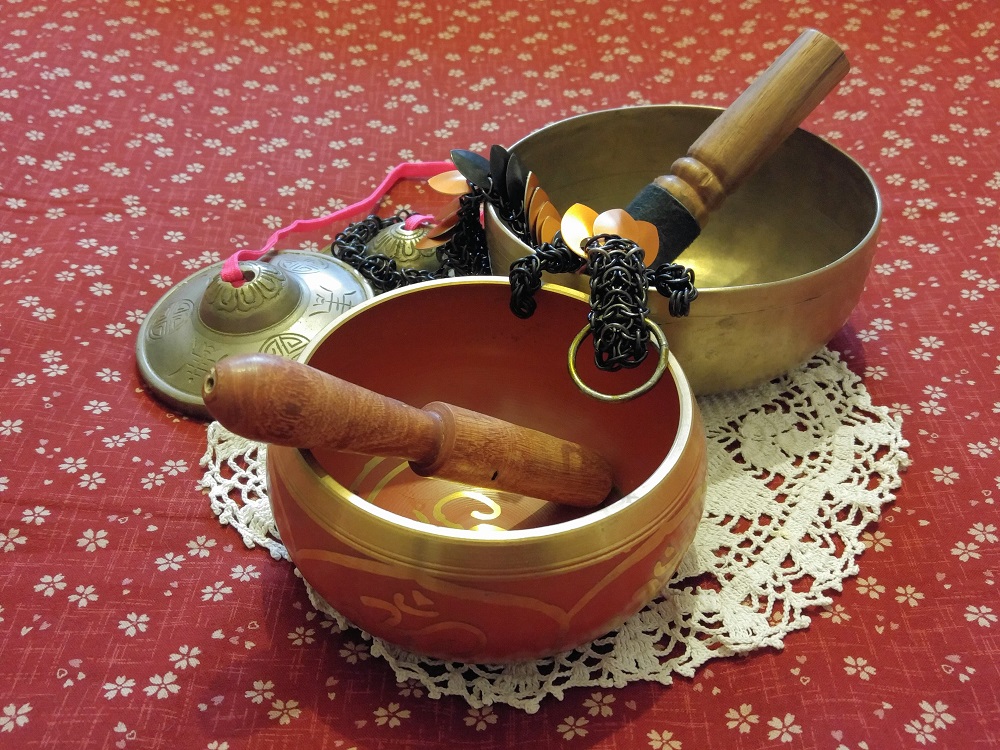 An orange and black striped dragon with black rings sitting amongst singing bowls and a tingsha, on top of a doily, atop a red sakura flower print bed.