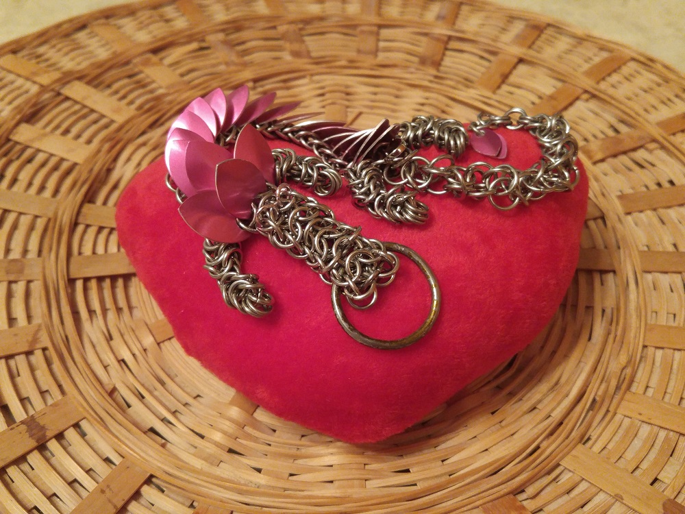 A pink dragon curled on top of a red plush heart, on top of a wicker basket.