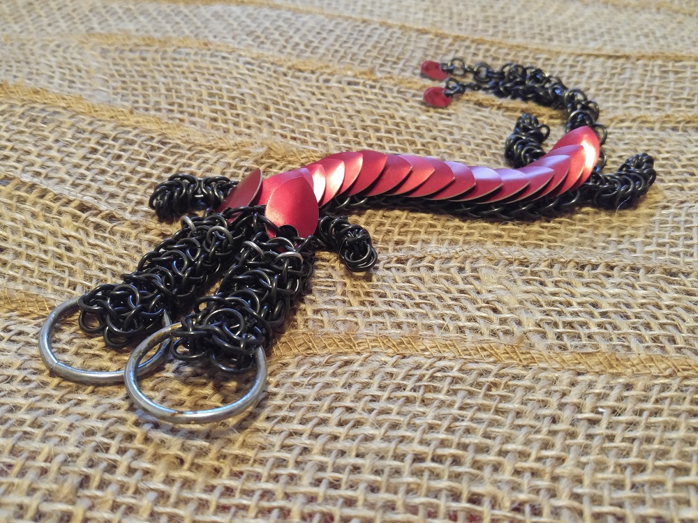 A two headed red dragon with black rings, and a split tail, laying on a light brown burlap fabric.