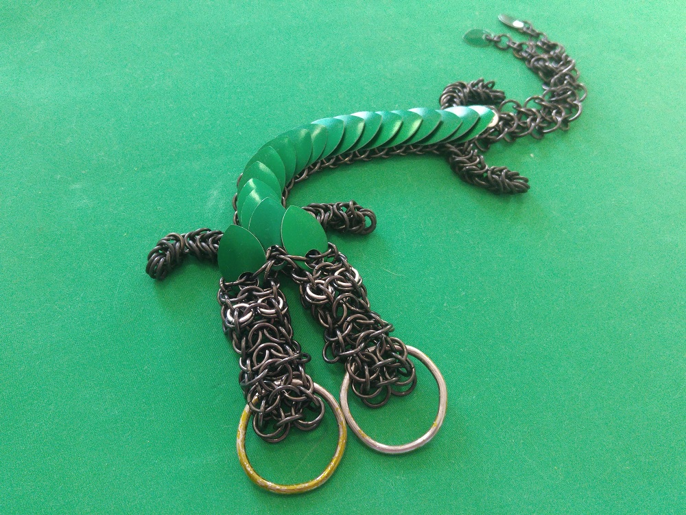 A green two headed dragon with black rings and a split tail, laying on a green surface.