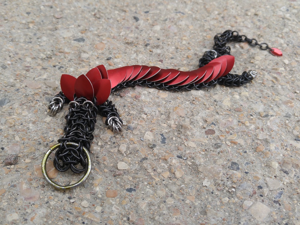 A red dragon with black rings but with silver feet, laying on a stone surface.