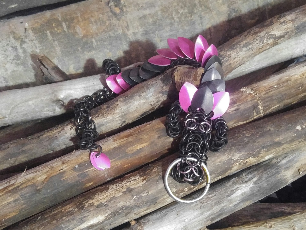 A bright pink and black striped dragon with black rings laying amongst wooden branches and logs.