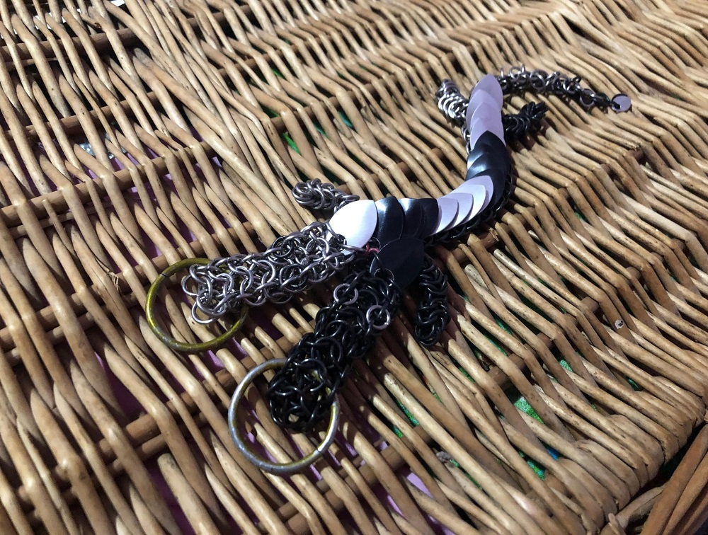 A two headed dragon with one side silver and one side black, with silver and black stripes and tail tip, laying on a light wicker basket.