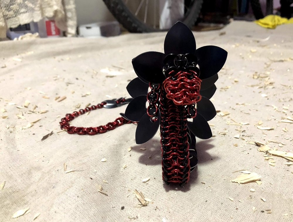 A large red and black dragon with black scales and wings, sitting amongst the wood chips of my creativity art nest, looking at the camera.