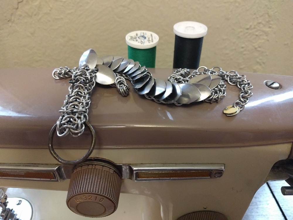 A silver dragon laying atop a brown sewing machine with green and black thread spools on it.