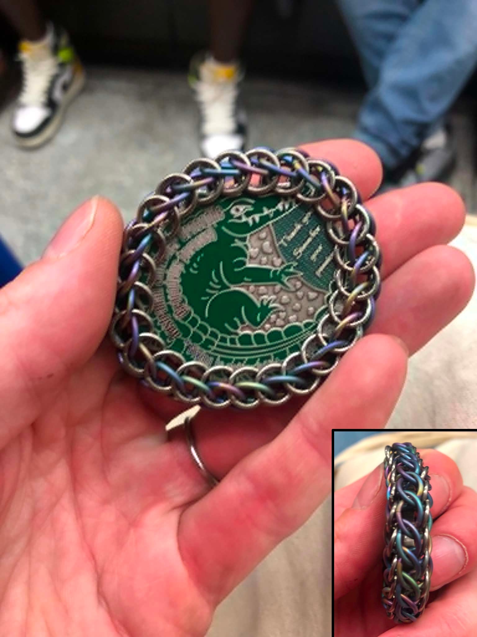 A two part photo, showing the wrapped coin from the face and the edge, taken on a train with people's legs in the background. The side rings are matte silver while the rainbow rings gradient between yellows to blues to purples, and the split persian gives an elegant series of eyes along the edge of the coin.