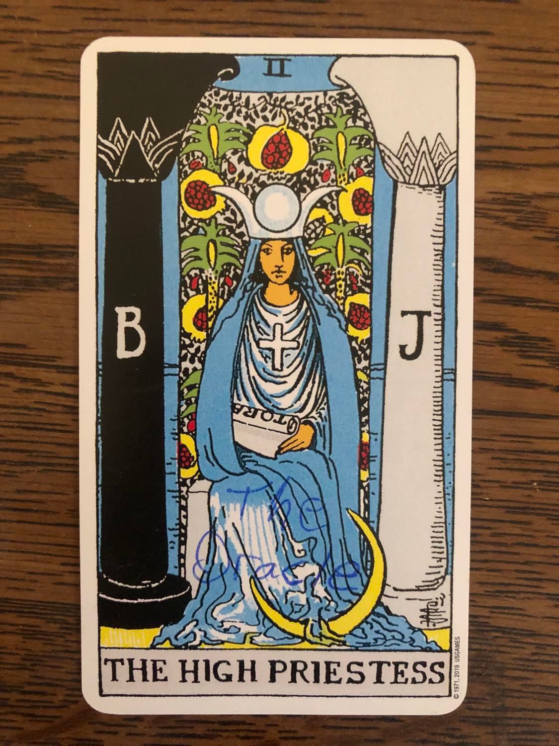 The high priestess card with the oracle written on it, laying on a wooden desk.