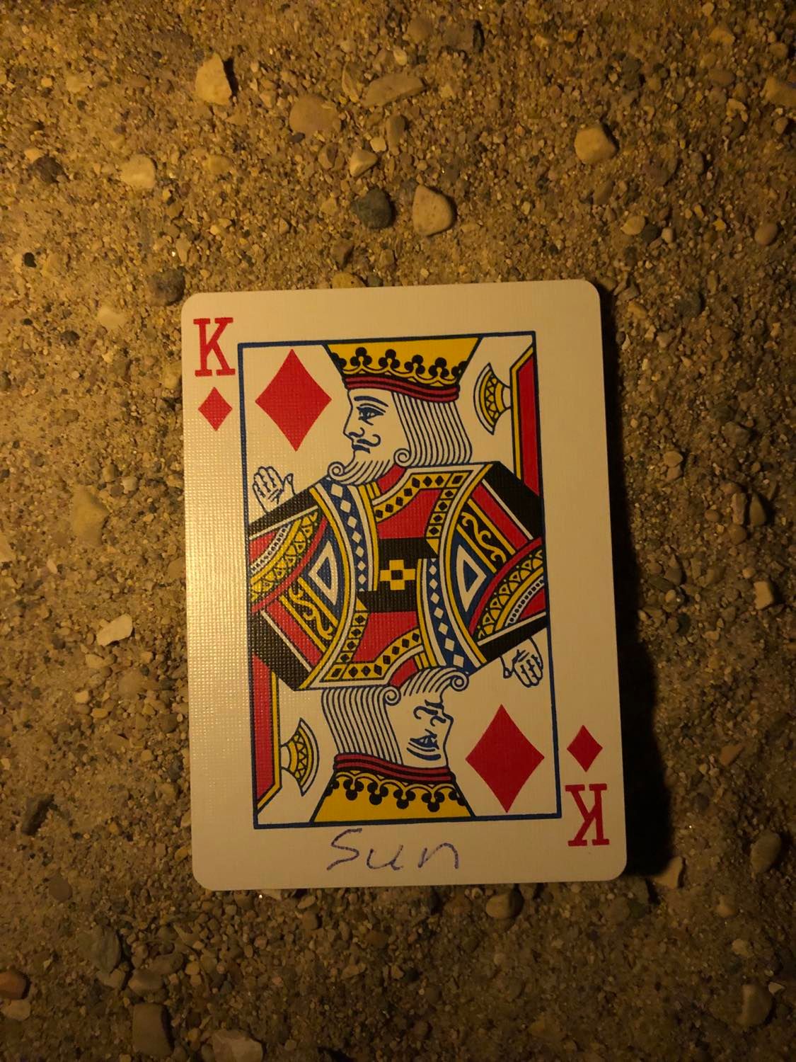 The king of diamonds with Sun written on it, laying on the darkened soil.