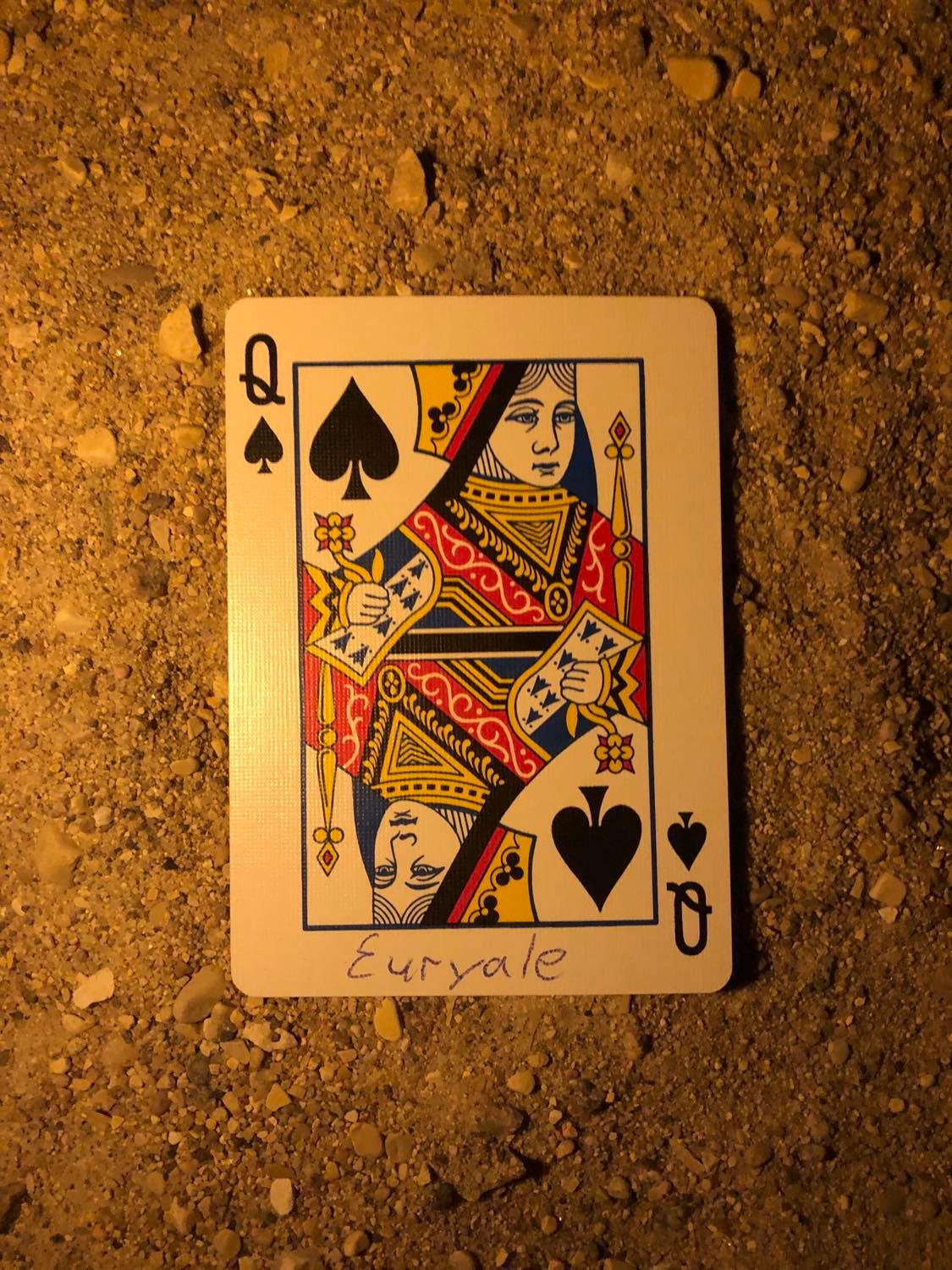 The queen of spades with Euryale written on it, laying on the darkened soil.