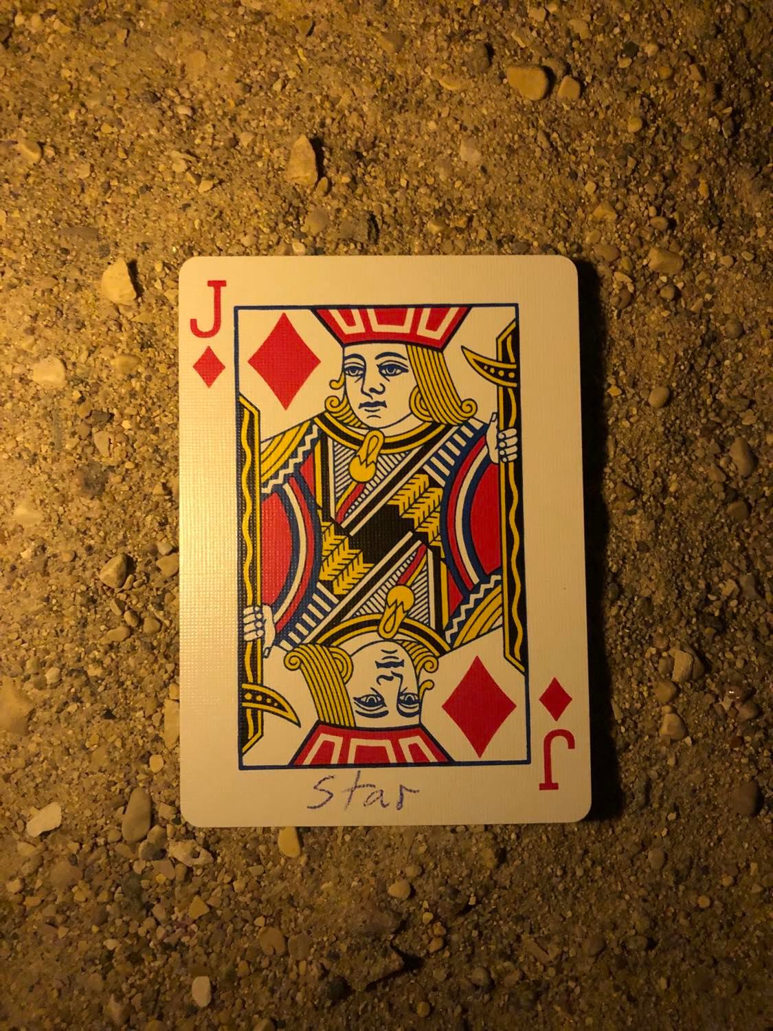 The jack of diamonds with Star written on it, laying on the darkened soil.