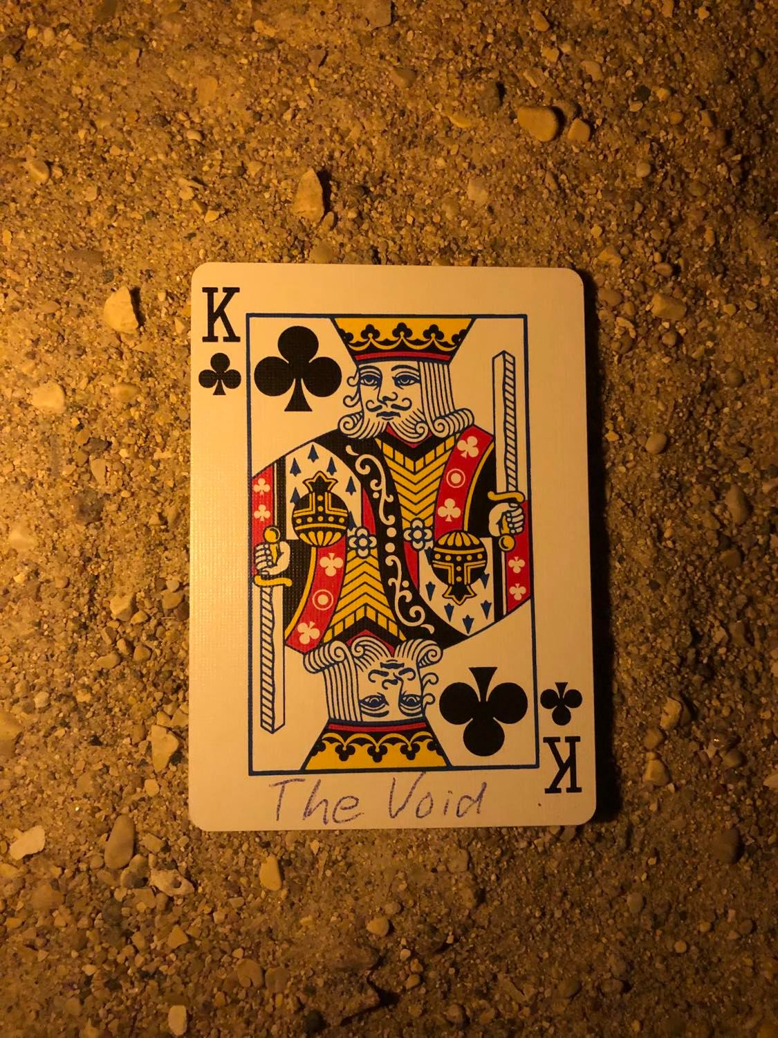 The king of clubs with The Void written on it, laying on the darkened soil.