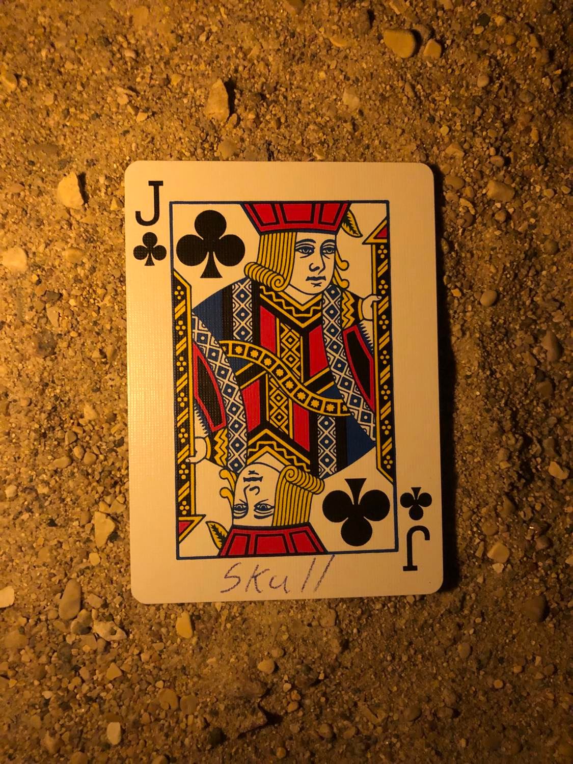The jack of clubs with Skull written on it, laying on the darkened soil.
