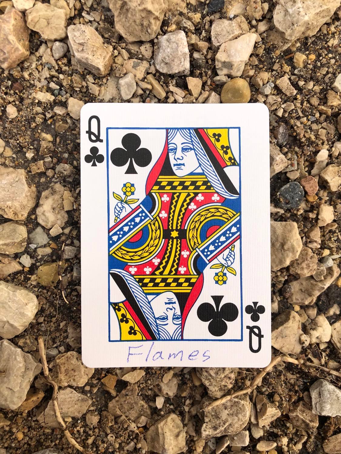 The queen of clubs with Flames written on it, laying on the gravel path.