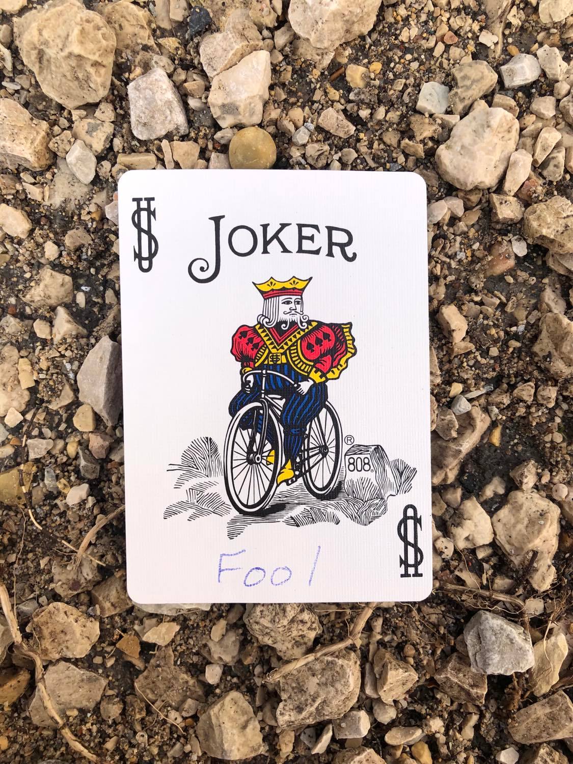 The joker with Fool written on it, laying on the gravel path.