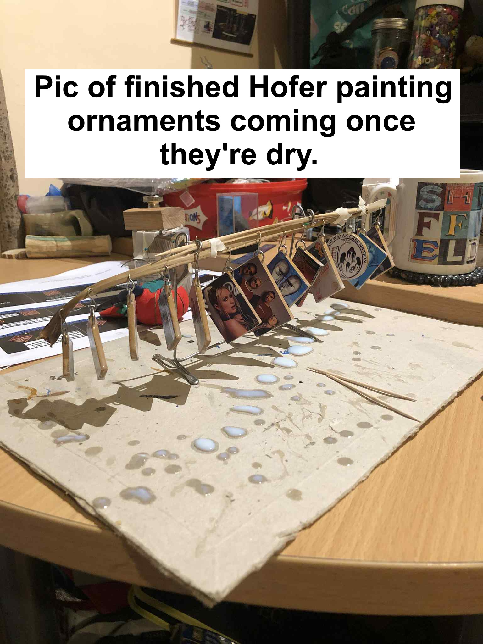 A photo of about a dozen miniature photos and images turned into little ornaments, dripping with varnish, and text over the image saying pic of finished hofer painting ornaments coming once they're dry.