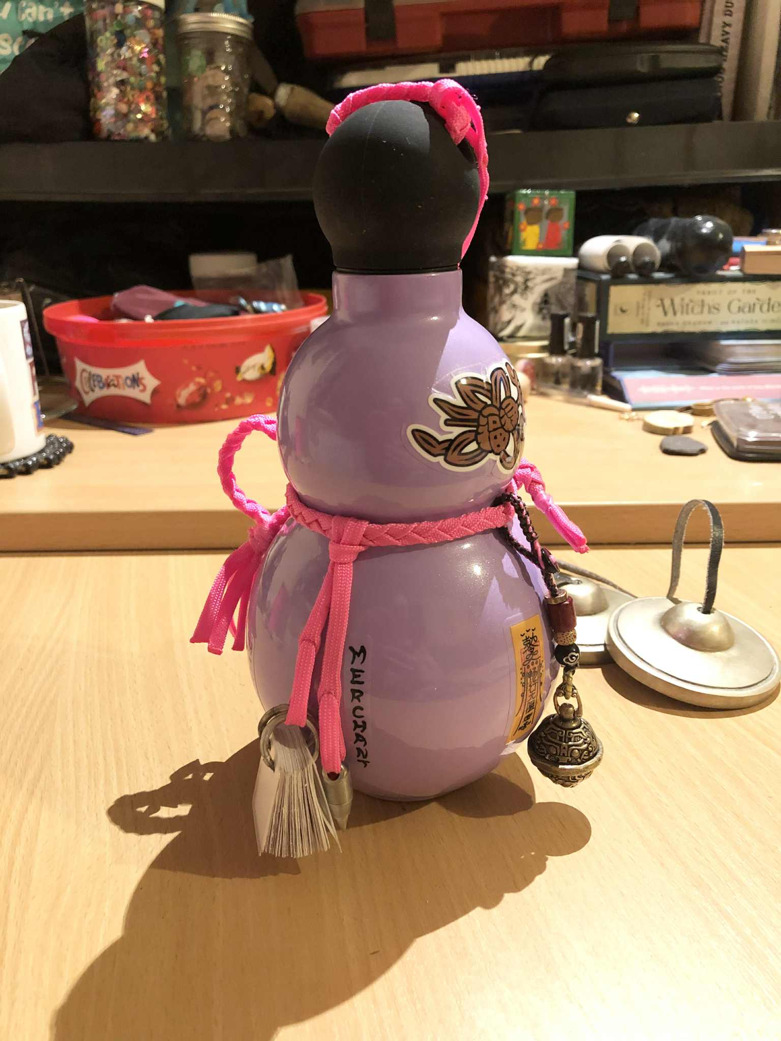 A lavender coloured gourd bottle depicting Japanese kanji for protection and balance, english text for Zebeth, and pink cords wrapped around it for carrying.