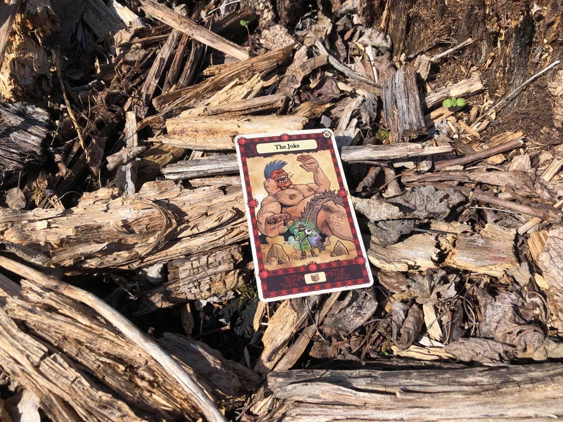 A giant laughing at a brave man, the card laying on the forest debris.