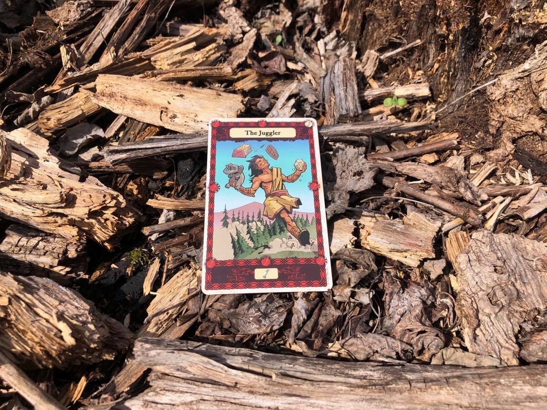 A man juggling objects, the card laying on the forest debris.