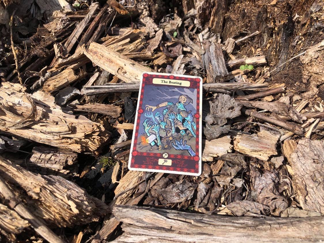 A man being grabbed by the undead, the card laying on the forest debris.