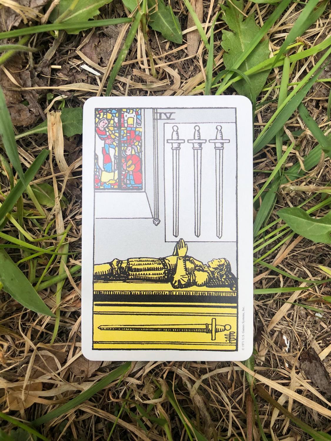 The Four of swords, upright, laying in the grass.