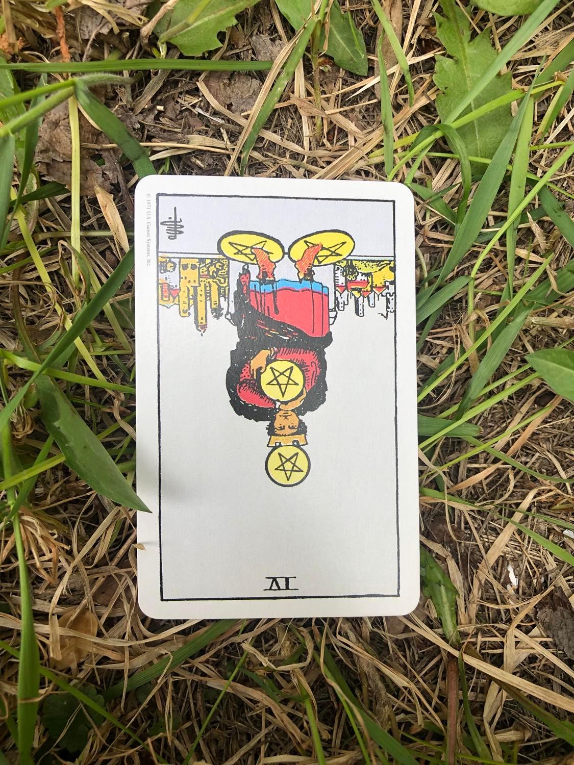 The Four of Pentacles, inverted, laying in the grass.