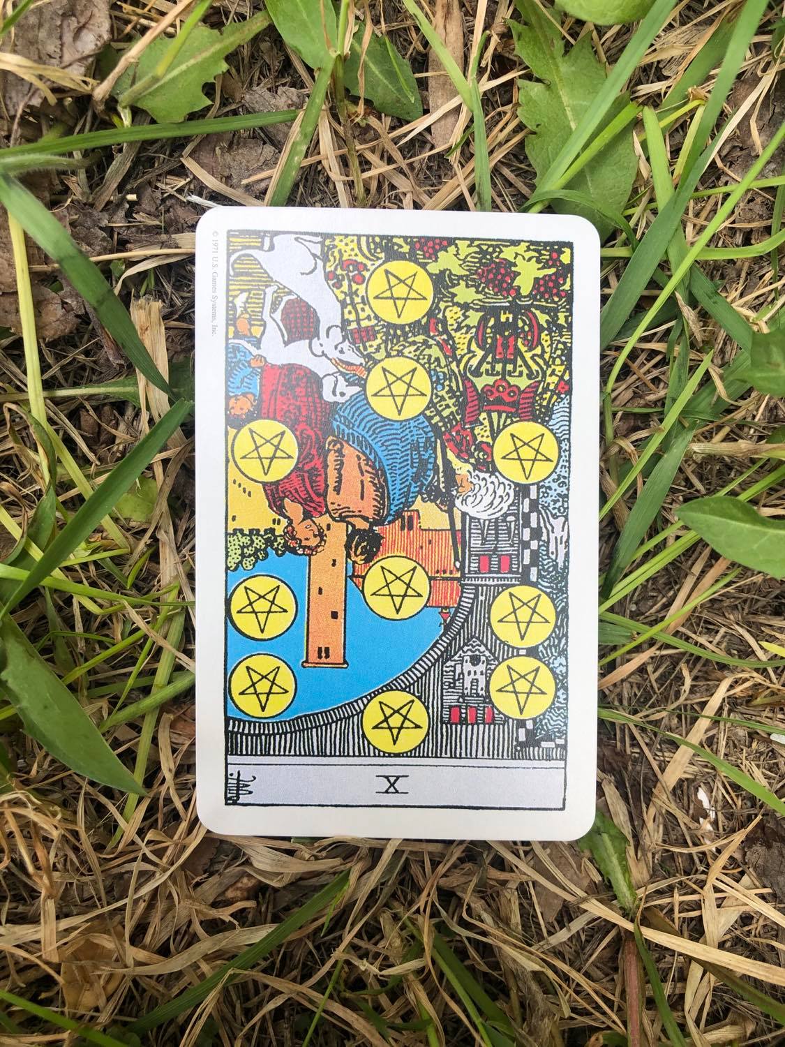 The Ten of Pentacles, inverted, laying in the grass.