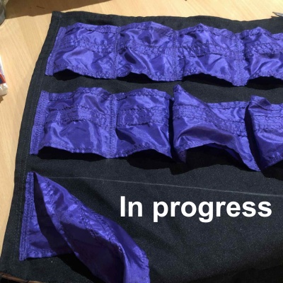 A partially completed black sheet with purple pockets sized to fit decks of cards, and the text in progress at the bottom right.