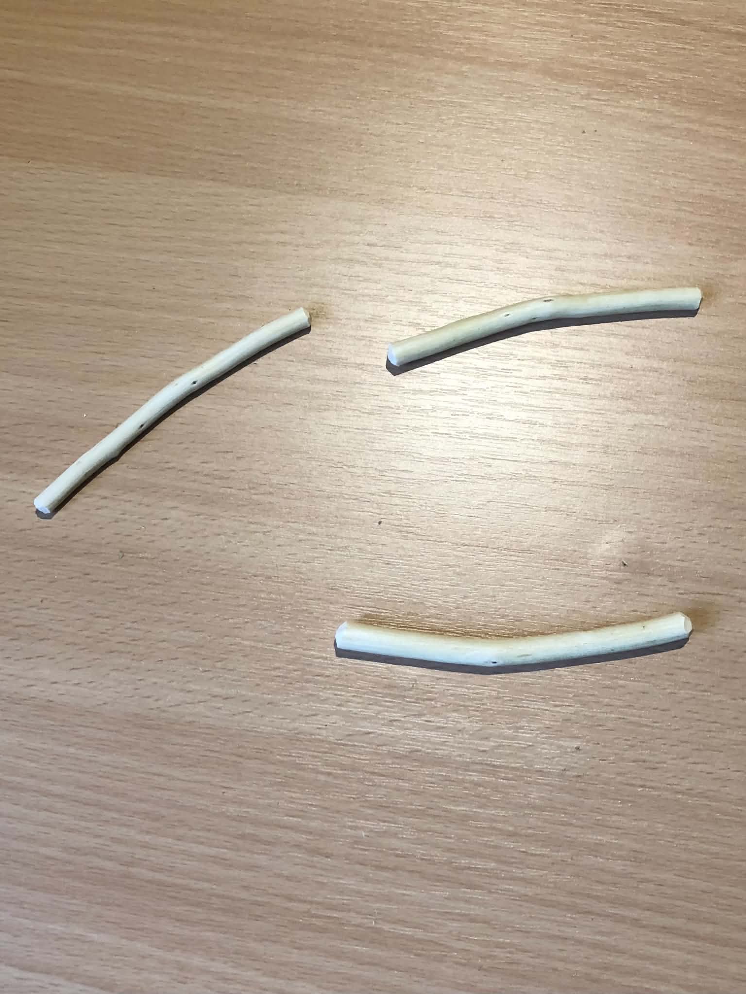 Three white peeled sticks, between about five to seven millimeters thick, all gently curved, and presently forming a cheerful smiling face on a wooden table.