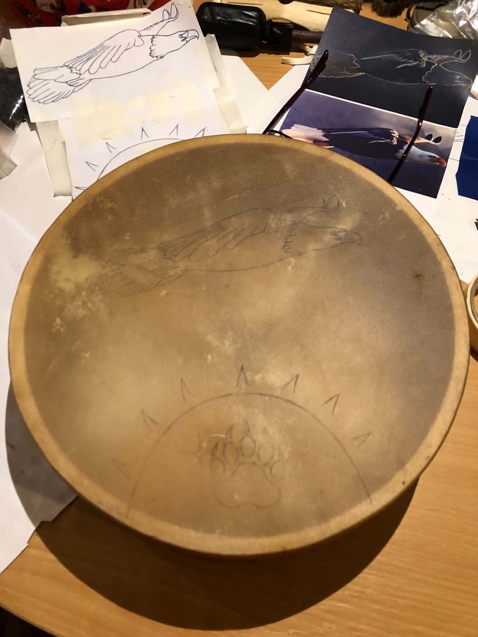 A leather hand drum with an eagle and sun motif stenciled on the face.