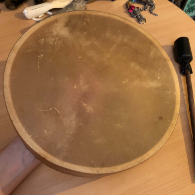 A tanned leather drum being held over a table, waiting to be painted.