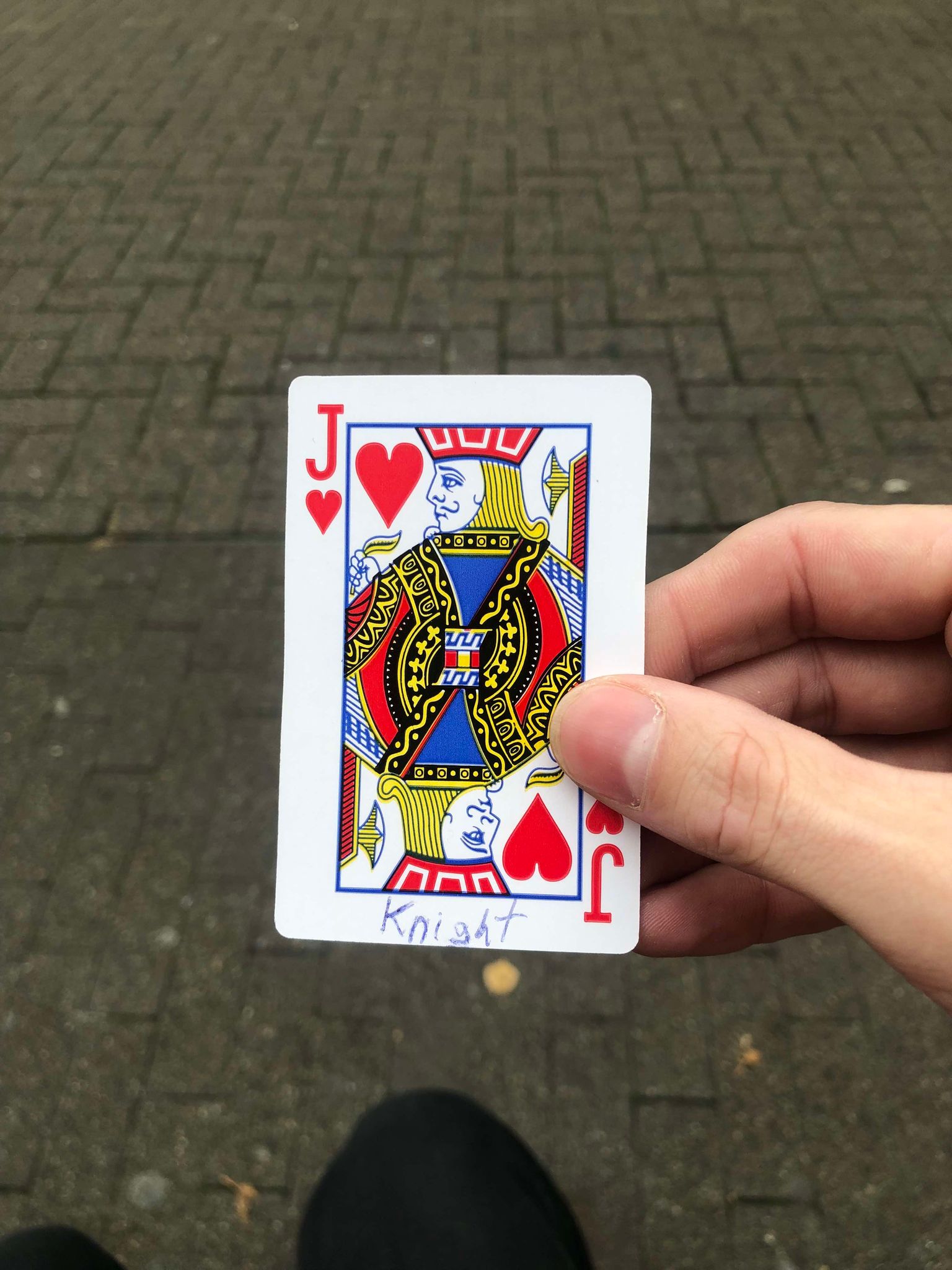 Sitting on a bench, a brick walkway in front of you, you hold the drawn card in front of you.