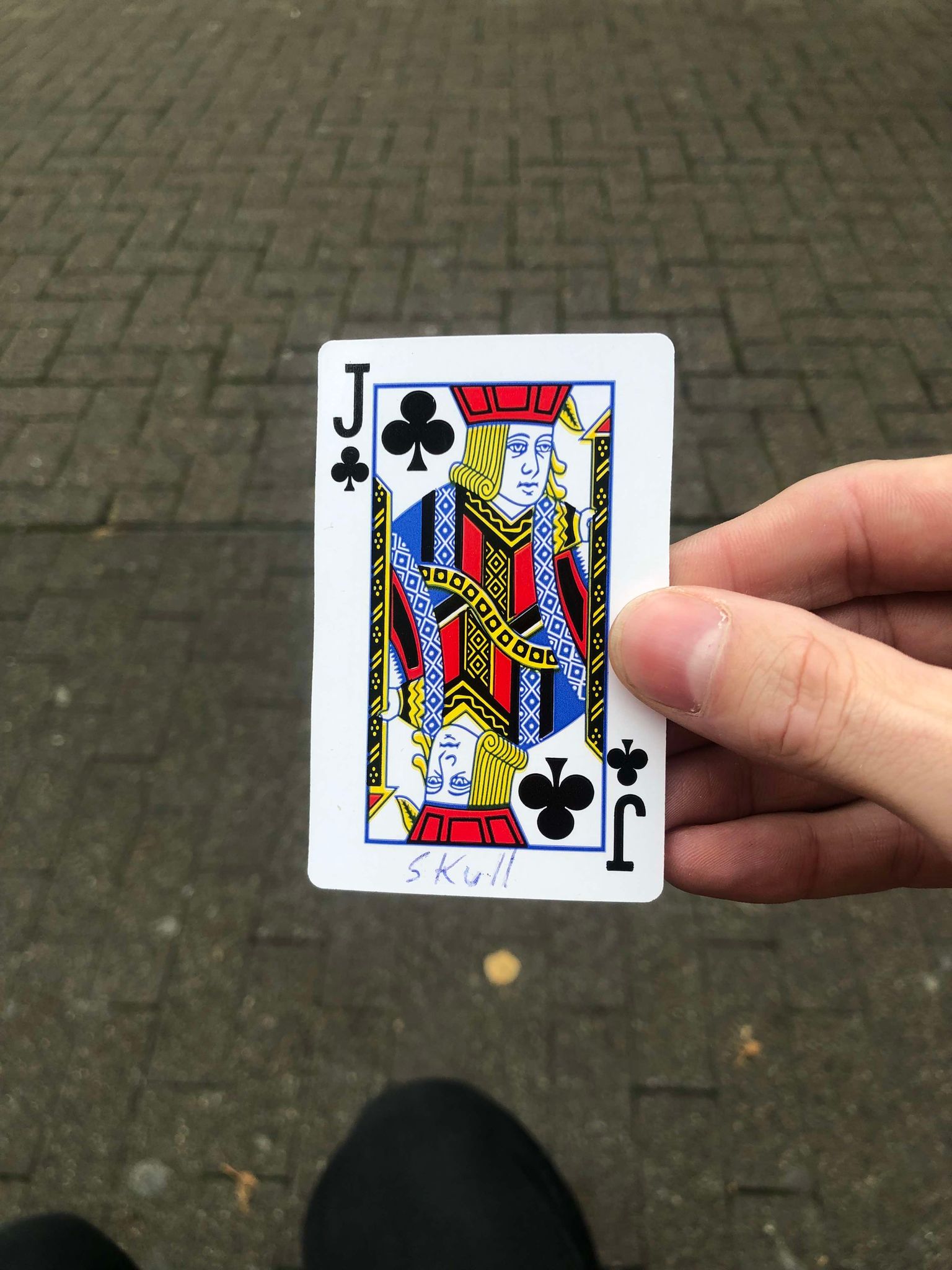 Sitting on a bench, a brick walkway in front of you, you hold the drawn card in front of you.