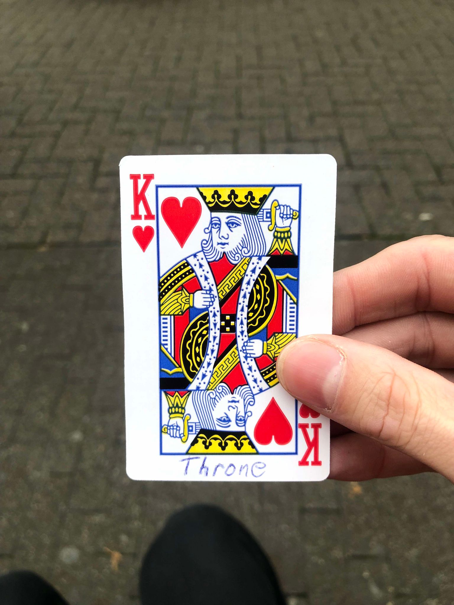 Sitting on a bench, a brick walkway in front of you, you hold the drawn card in front of you.