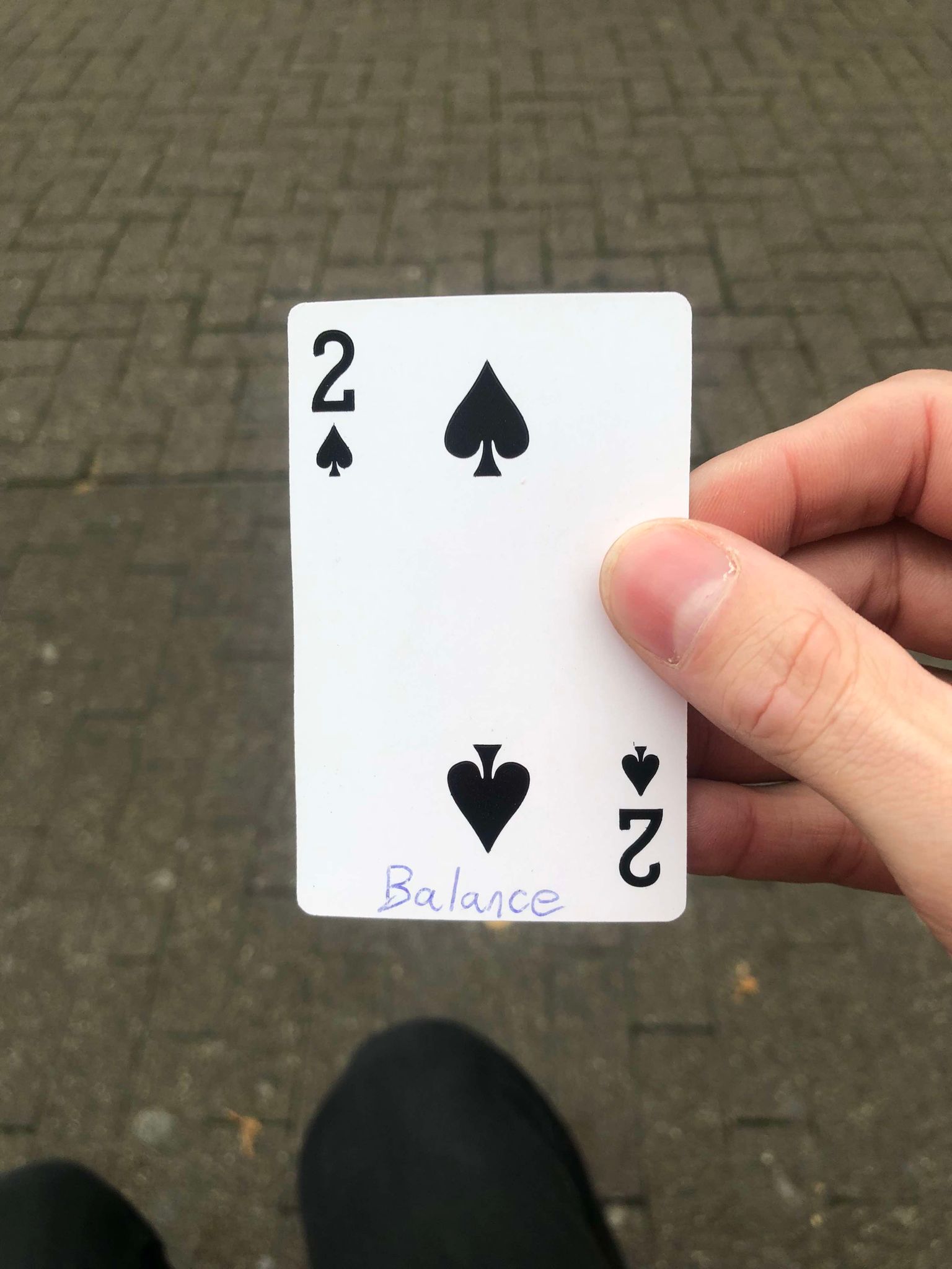 Sitting on a bench, a brick walkway in front of you, you hold the drawn card in front of you.