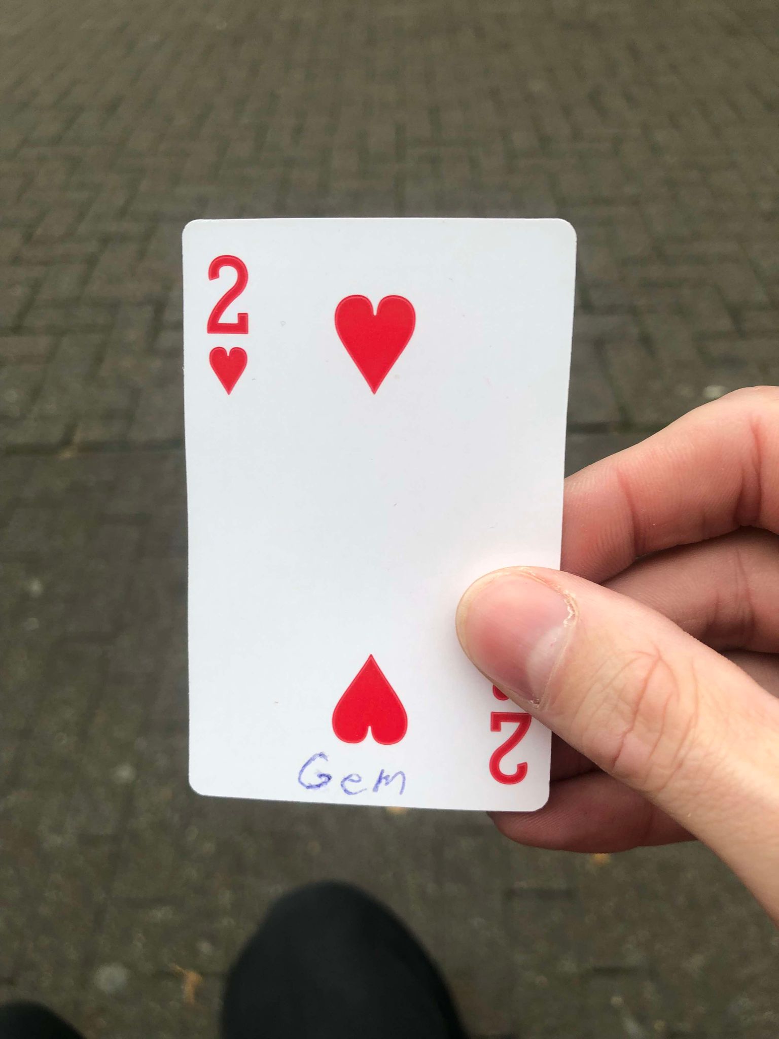 Sitting on a bench, a brick walkway in front of you, you hold the drawn card in front of you.