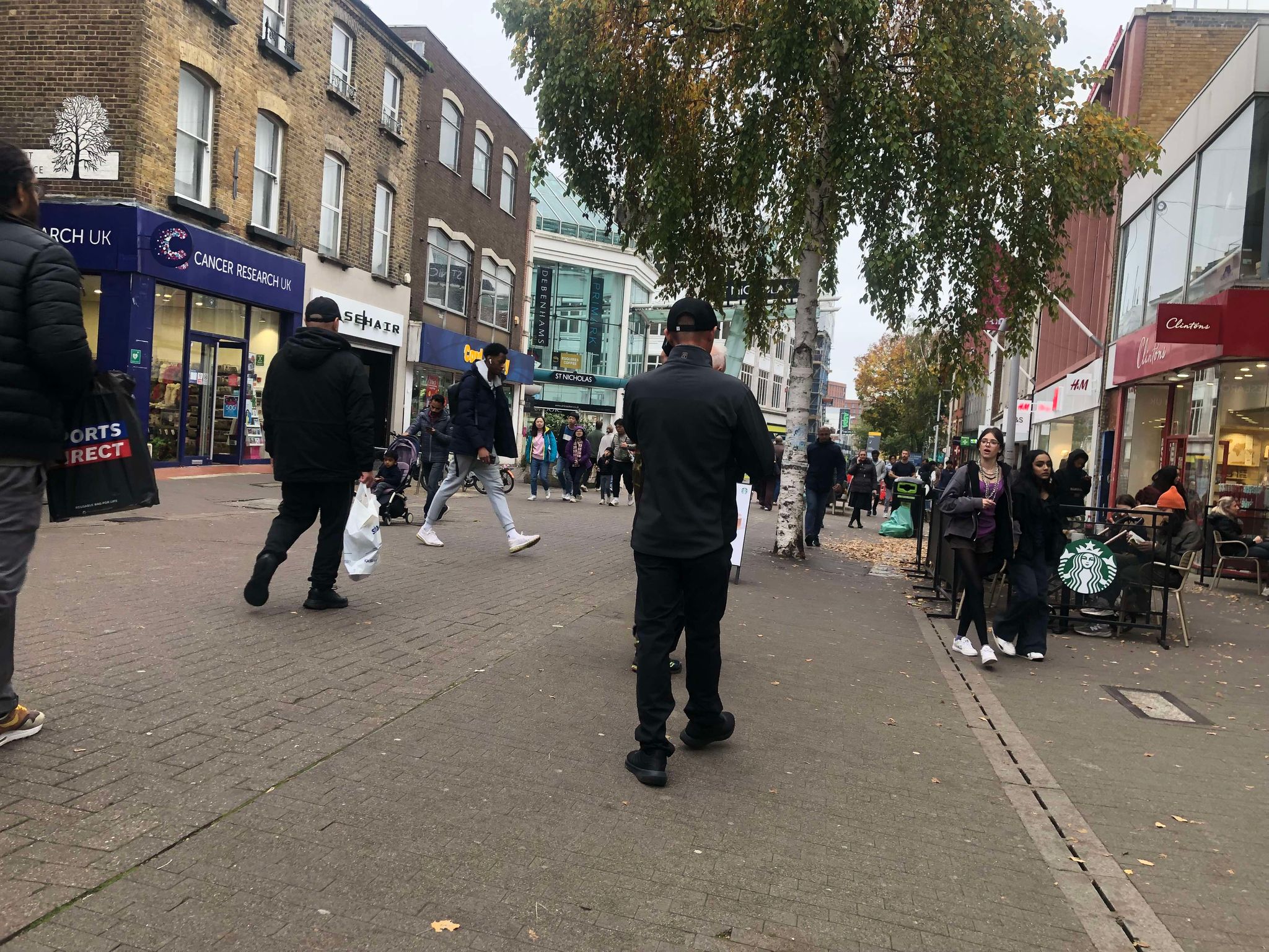 A man walking away from the camera on a bustling street full of shops.