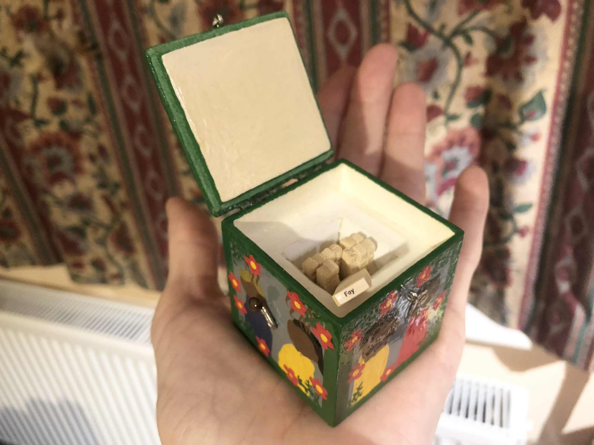 Beneath the jester, a set of twelve wooden sticks are arranged in the center. One of them has been pulled up, the underside showing the word Fey, the type of creature that will now be summoned with the opening of the box.