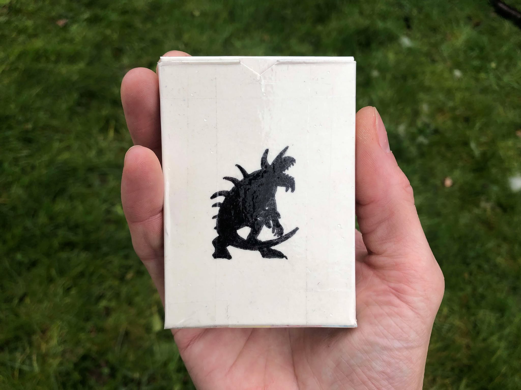 A deck of cards, being held in a grassy area, with the silhouette of a tarrasque on the face of it. What might happen if a card is drawn? Should we try?