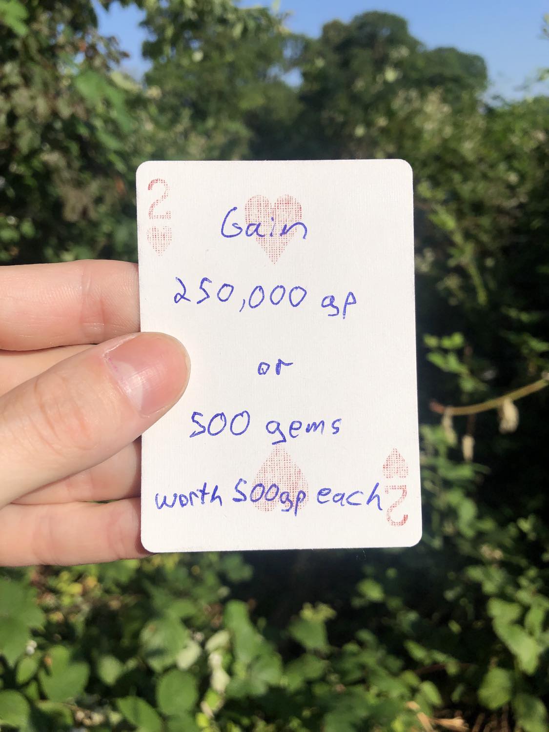 The two of hearts, held with the trees and foliage behind. Gain 250,000 gp, or 500 gems worth 500 gp each.