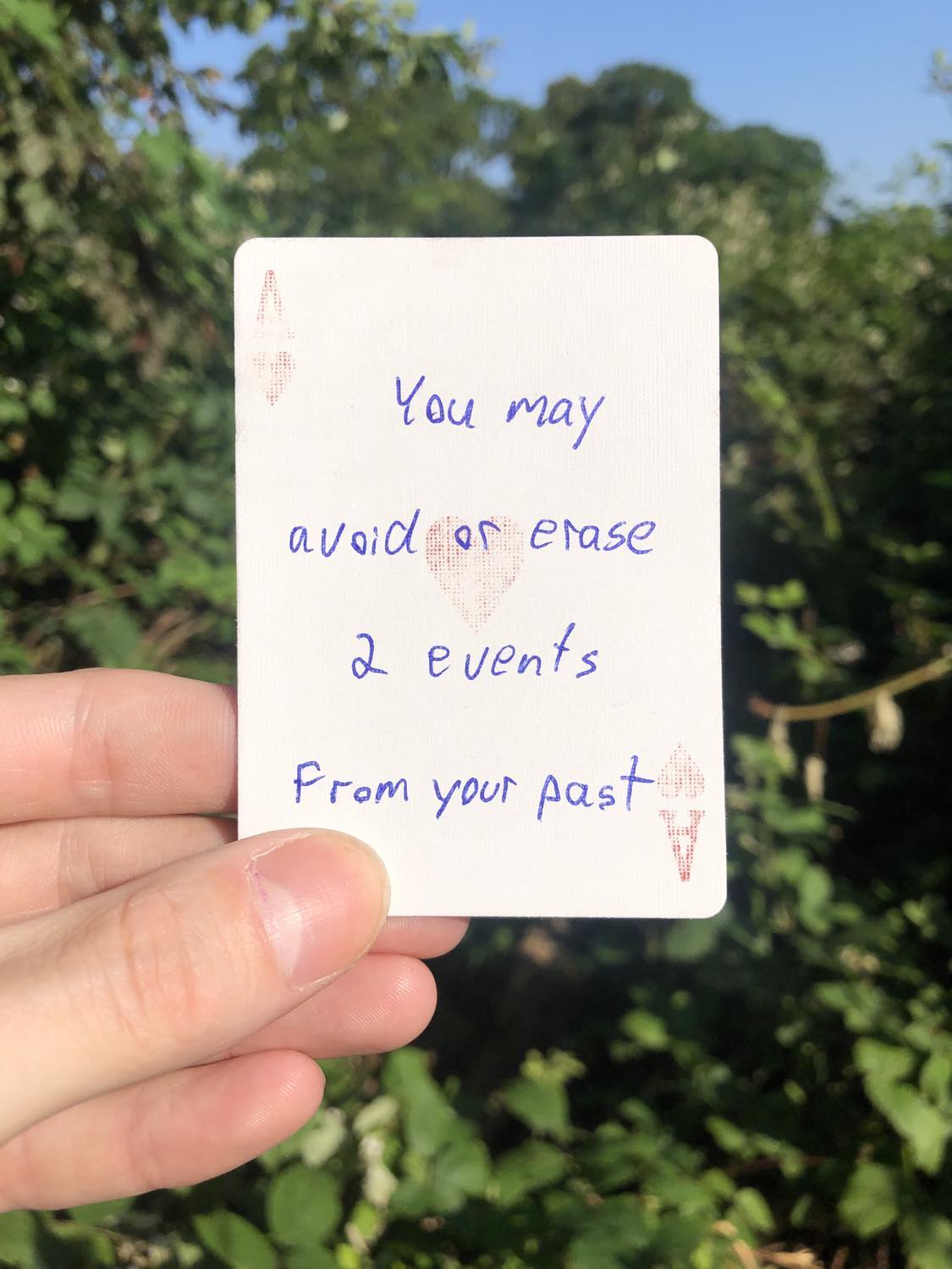 The ace of hearts, held with the trees and foliage behind. You may avoid or erase 2 events from the past.